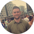 Chris-Hogan-Husky-Customer A man in a green polo shirt stands outdoors in front of a cityscape with modern buildings, people, and recent concrete resurfacing visible in the background.