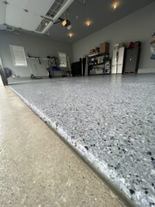 Low-angle view of a garage after resurfacing a garage floor with epoxy, featuring storage shelves, a refrigerator, bicycles, and tools neatly arranged along the walls.