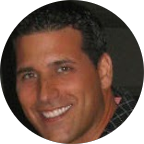 Scott Barone-Husky-Tetstimonial-Happy Customer A man with short dark hair smiling, wearing a dark shirt, photographed against a dark background that subtly resembles concrete resurfacing.