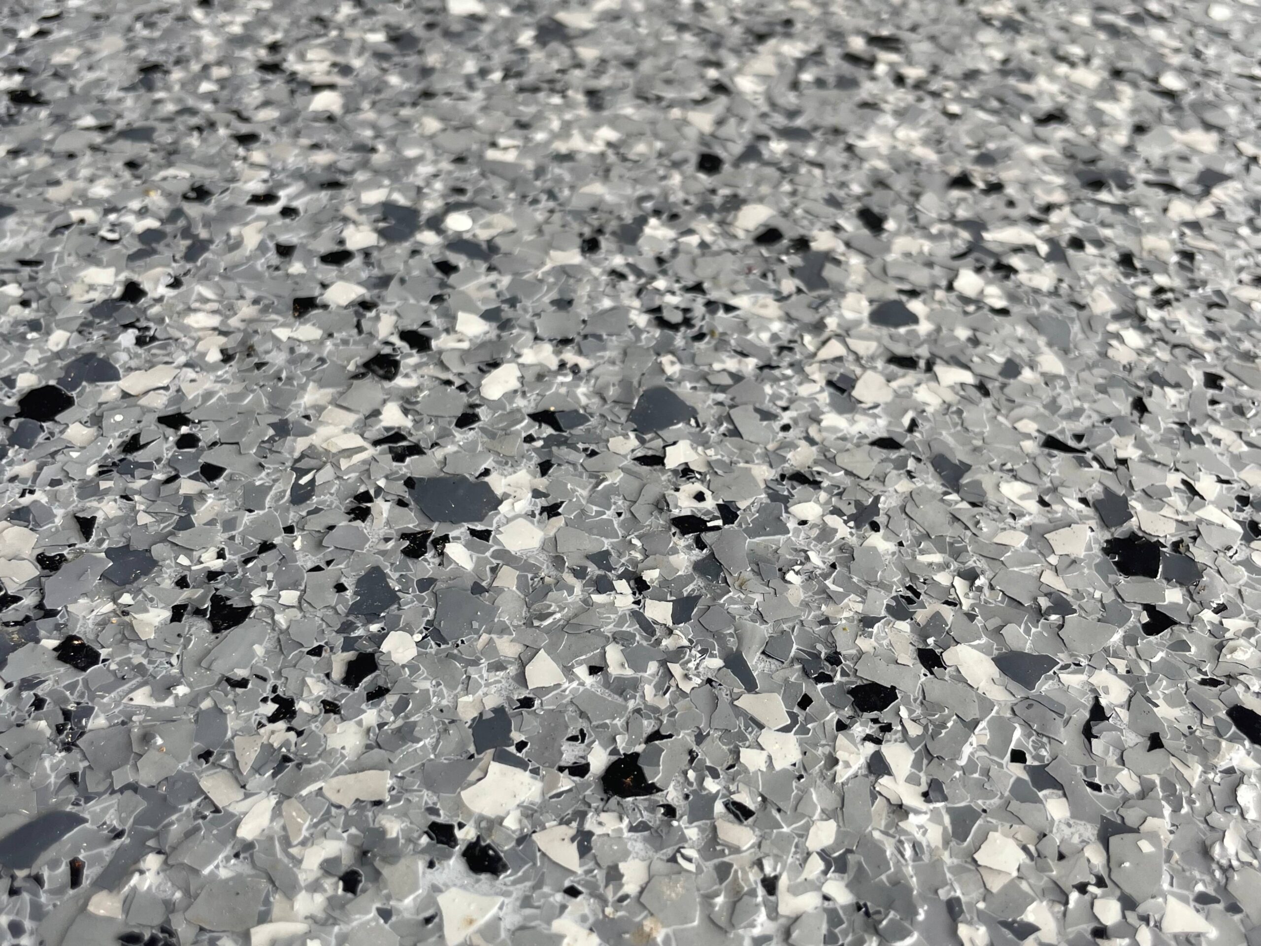 Close-up of a speckled epoxy floor with various shades of gray, black, and white flakes creating a textured surface.